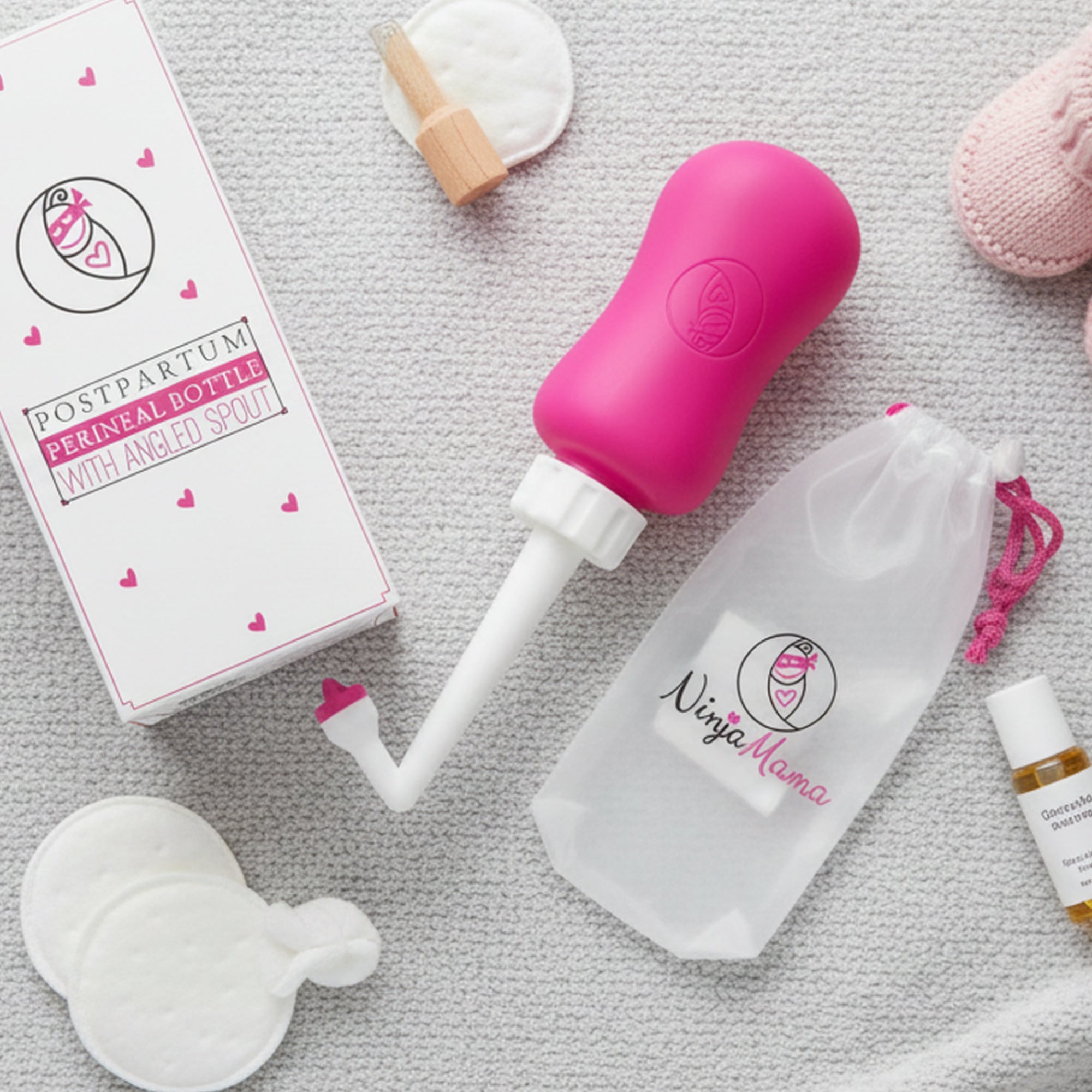 Pink ninja mama peri bottle for postpartum care product with packaging and accessories on a textured surface